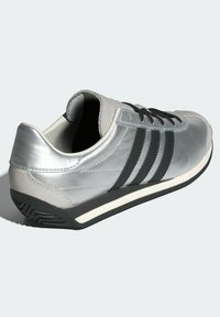 Silver athletic shoe with black accents, featuring a sleek design, smooth texture, rounded toe, and a contrasting white sole.