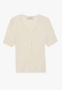Haut à manches courtes de couleur beige clair en tissu côtelé, doté d'un décolleté en V et d'une patte de boutonnage à trois boutons à l'avant.