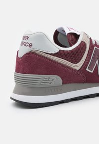 Burgundi velúr és hálós sneaker szürke kiegészítőkkel, fehér sarokkal és fekete gumitalppal. Az alján dombornyomott logó található.