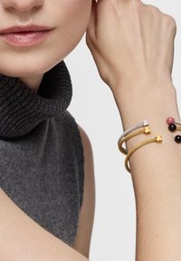 Trzy bransoletki wykonane z elastycznego metalowego drutu w odcieniach szarości, żółci i złota, ozdobione metalowymi akcentami w kształcie niedźwiedzi oraz małymi koralikami.