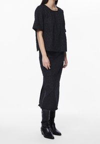 Woman wearing a black textured short-sleeve top and matching midi skirt with subtle heart patterns, paired with black mid-calf leather boots.