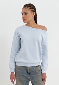 Lys blå hettegenser med off-shoulder design, lange ermer, ribbede mansjetter og avslappet passform, parret med falmede blå jeans.