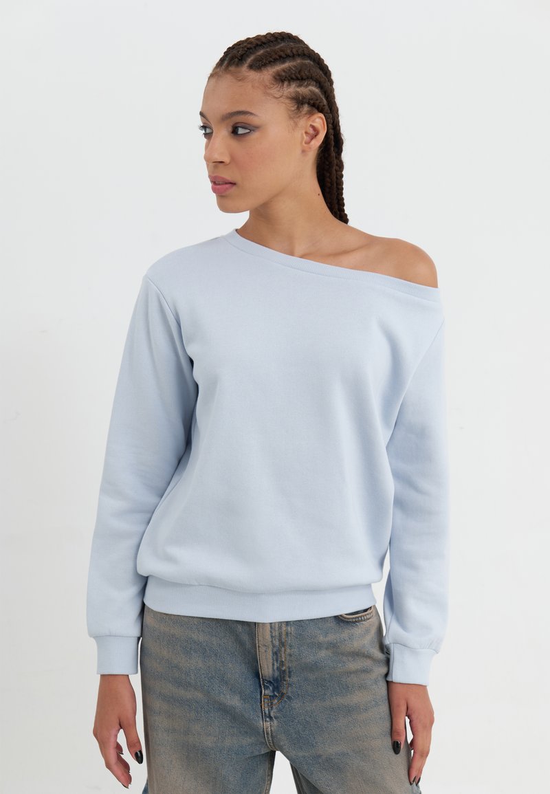 Lys blå hettegenser med off-shoulder design, lange ermer, ribbede mansjetter og avslappet passform, parret med falmede blå jeans.