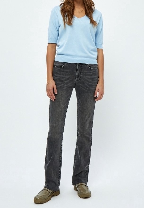 Světle modrý svetr s výstřihem do V, šedé rozšířené džíny a olivově zelené boty. Svetr má krátké rukávy; džíny mají klasický design s pěti kapsami.