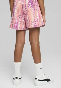 Pantalones cortos de colores rosa y púrpura con un ajuste relajado, combinados con zapatillas blancas y calcetines blancos a juego que presentan un logo negro.