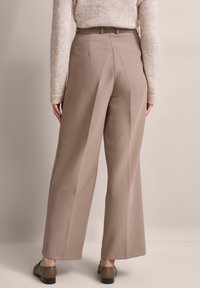 Beige wide-leg trousers with a high waist, pleated front, and belt loops, paired with a light sweater, seen from the back.