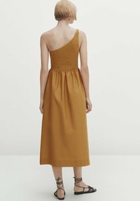 Robe sans manches jaune moutarde avec un corsage ajusté smocké et une jupe fluide. Longueur à la cheville avec une silhouette décontractée et un design minimaliste.