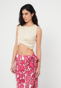 Μπεζ αμάνικη μπλούζα με στριφτό μπροστινό σχέδιο, σετ με μακριά, ροζ και λευκή φούστα με σχέδιο, που διαθέτει πλαϊνή σκίσιμο και φιόγκο στη μέση.