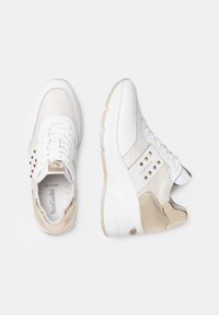 White and beige sneakers with a mesh upper, metallic accents, decorative studs, and a chunky sole design. Neat laces and logo detail visible.