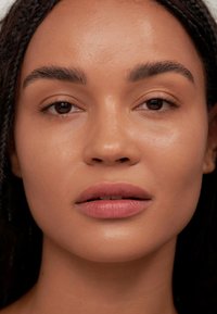 Primer plano de un rostro con piel clara, labios ligeramente contorneados en un tono natural, cejas bien definidas y cabello oscuro trenzado que enmarca la cara.
