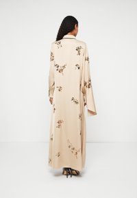 Hosszú bézs selyemruha virágos hímzéssel, hosszú ujjal, gallérral és légies fazonnal. Az anyag sima textúrájú.