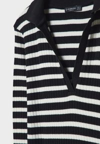 Pull en maille côtelée à rayures horizontales noires et blanches avec un col noir et un décolleté en V.