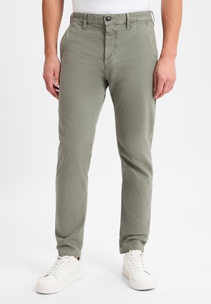 Olive green chinos with a straight cut, five pockets, and a button closure, paired with white sneakers. Smooth fabric, lightweight design.