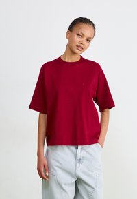 Tricou scurt cu maneci, de culoare burgundă, din bumbac fin, cu guler rotund și un accent mic cu logo pe piept. Asortat cu pantaloni cargo de culoare bleu deschis.