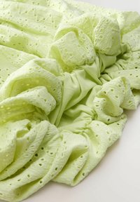 Tissu vert clair à volants avec des motifs découpés, doté d'une doublure intérieure lisse. Texture douce avec des fronces et un design fluide continu.