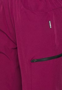 Vaaleanliilat vaellushousut, joissa on vetoketjullinen tasku ja logotäppä. Kangas näyttää kevyeltä ja tekstuuriltaan, suunniteltu liikkuvuutta ja mukavuutta varten.