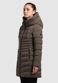Abrigo acolchado marrón con un cuello alto y capucha ajustable, que presenta un diseño acolchado, cremallera frontal y dos bolsillos laterales con cremallera.