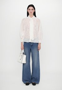Chemisier floral blanc en voile avec un nœud, jeans en denim bleu larges et un petit sac à main blanc avec des accents noirs. Chaussures noires à enfiler.
