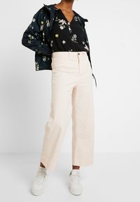 Un pantalon large rose clair associé à un blouse noire à fleurs et à un coupe-vent à fleurs sombres. Des baskets blanches complètent l'ensemble.