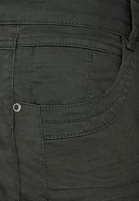 Jean en denim vert foncé avec une poche arrière ornée de coutures discrètes, un bouton métallique en accent, et une texture lisse.