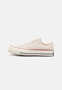 Beige kanvas lave sneakers med hvit gummisåle, røde og marineblå striper. Har runde lisser og metalløyer. Klassisk design.