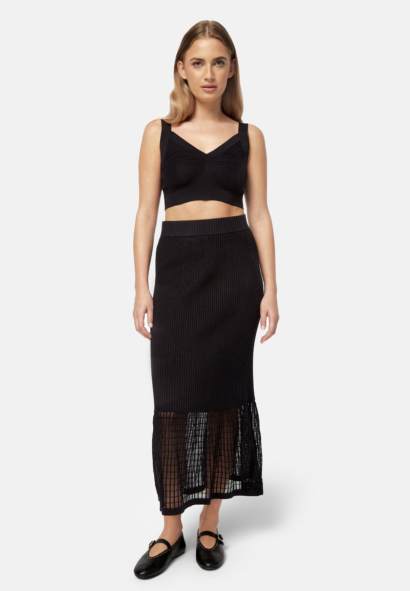 Mustmustö värviga ribakudumist crop top ja pikk seelik, millel on läbipaistev pitsäär. Komplekti kuuluvad mustad lamedad kingad.