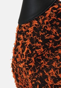 Tessuto nero testurizzato con fili arancioni, caratterizzato da un accento in pelle nera liscia. Il design ha un aspetto fluffy a causa delle fibre sciolte.