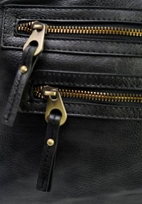 Zwarte leren tas met twee messing ritsen met gestructureerde treklippen en goudkleurige metalen accenten rondom de zakken.