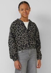 Grijze cropped hoodie met een zwart luipaardpatroon. Voorzien van een rits aan de voorkant en een trekkoordkap. Gepaard met grijze jeans.