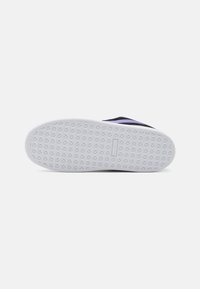Semelle de chaussure en caoutchouc blanc avec un motif texturé pour l'adhérence. Caractérisée par une tige noire avec des accents violets, conçue pour un usage décontracté.