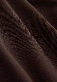 Dunkelbrauner Stoff mit feiner Strickstruktur, dargestellt in weichen Falten, die sanfte Schatten und Highlights schaffen.