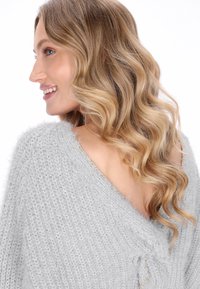 Grijze gebreide sweater met een losse pasvorm en V-halsontwerp, met een zachte textuur en een decoratieve strikdetail aan de zijkant.