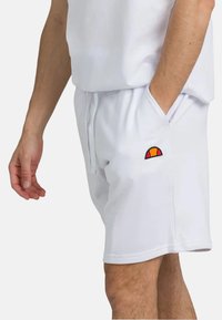 Pantaloni corti bianchi realizzati in un tessuto morbido, dotati di tasche laterali e di un piccolo logo ricamato multicolore sul lato sinistro.