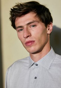 Gray checkered button-up shirt with a pointed collar, featuring small buttons and a smooth texture, worn by a young man.