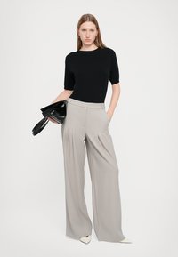 Zwarte top met korte mouwen gecombineerd met lichtgrijze, hoge taille wijde broek. Het model houdt een zwarte handtas vast, en de puntige witte hakken zijn zichtbaar.