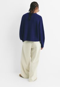 Mornarsko plavi rebrasti pleteni pulover sa širokim, skraćenim siluetom i širokim rukavima, uparen s bež širokim hlačama i smeškim obućom.