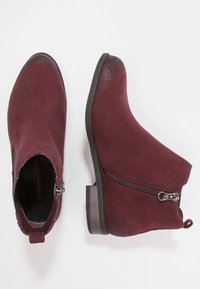 Par de botas cortas de ante burdeos con cremalleras laterales y tacones bajos en un fondo blanco.