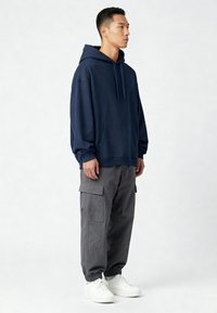 Felpa con cappuccio blu navy con tasca frontale, abbinata a pantaloni cargo grigi con tasche laterali e polsini elasticizzati, indossata con sneakers bianche.