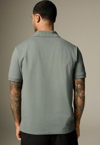 Grå kortærmet polo-shirt med standard krave, glat tekstur og et rent design. Har diskrete rulleærmer og en lige kant.