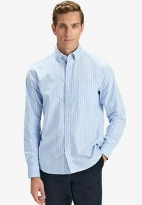 Vaaleansininen pitkähihainen paita, jossa on valkoisia pystysuoria raitoja, nappikaulus, yksi rintatasku ja sileä puuvillakangas.