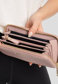 Portafoglio texturizzato rosa con zip dorata, diverse fessure per carte e interno nero. Tenuto in una mano, che mette in mostra i suoi scomparti e il design.