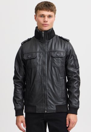 Chaqueta de cuero negro con cierre de cremallera, dos bolsillos en el pecho, puños acanalados y un cuello alto con hombreras. Textura suave.