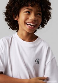 Camiseta de algodón blanca con un pequeño logo gris "cK" en el lado izquierdo del pecho, cuello redondo y mangas cortas, con un corte relajado.