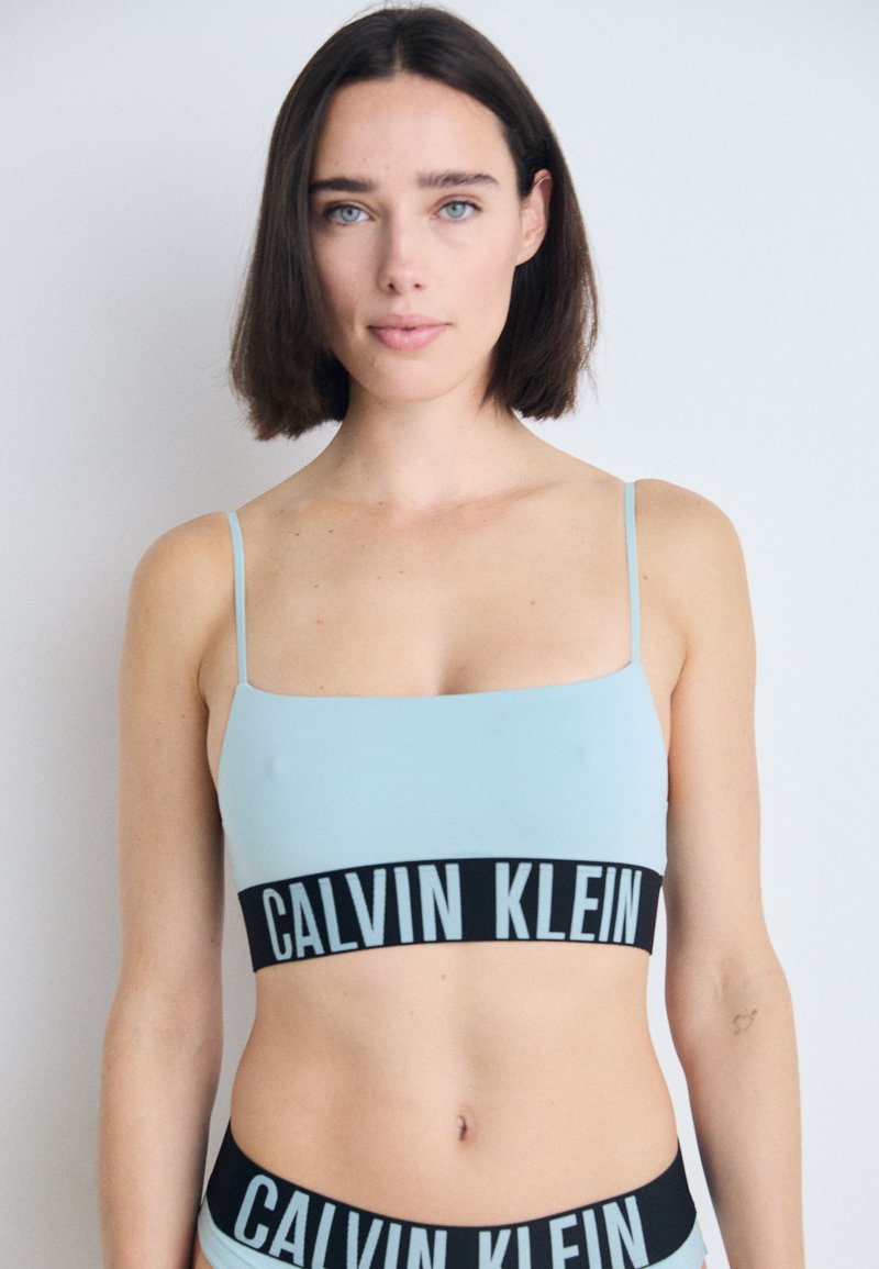 Šviesiai mėlynas apkarpytas bralette su plonomis petnešėlėmis ir juoda juostele, ant kurios užrašyta "CALVIN KLEIN" šviesiai mėlyna spalva. Lygus, tamprus audinys.