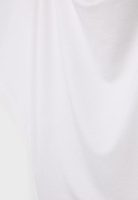 Tissu en coton blanc et doux qui drape avec fluidité. La surface semble légèrement texturée avec des plis subtils, mettant en valeur un design à la coupe décontractée.