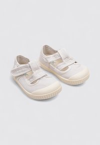 Chaussures en toile beige clair avec un bout renforcé, des fermetures à bande Velcro et des découpes sur les côtés ; semelle extérieure en caoutchouc texturé.