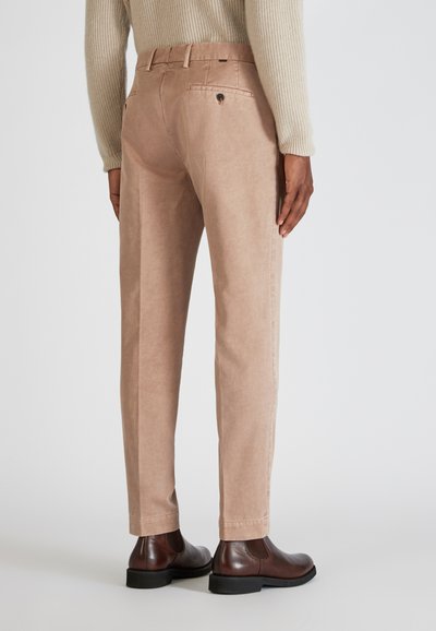 Beige Baumwollmischungshosen mit geradem Schnitt, ausgestattet mit Gesäßtaschen und Gürtelschlaufen. Getragen mit dunkelbraunen Leder-Stiefeletten.