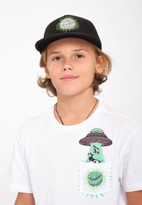 Casquette noire avec logo vert ; T-shirt blanc avec un graphique coloré d'extraterrestre et de vache sur la poche ; col rond, coupe décontractée.