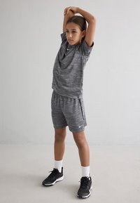 Pelēka sporta apģērba komplekts, kas sastāv no īsām piedurknēm tērpa un šortiem, izgatavots no melnākas materiāla, kombinēts ar melniem sporta apaviem un baltiem zeķēm.