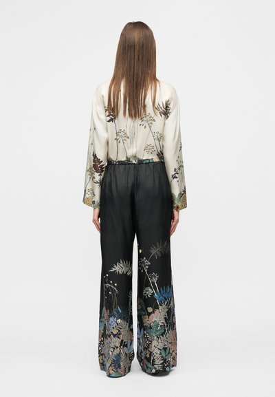 Μεταξωτό πουκάμισο με κεντήματα λουλουδιών, συνδυασμένο με μαύρο παντελόνι φαρδιάς γραμμής με πολύχρωμα μοτίβα φύλλων στο τελείωμα.